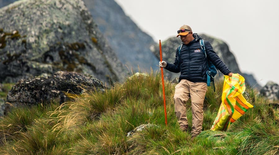 A trekker carrying a rubbish bag along a mountain trail